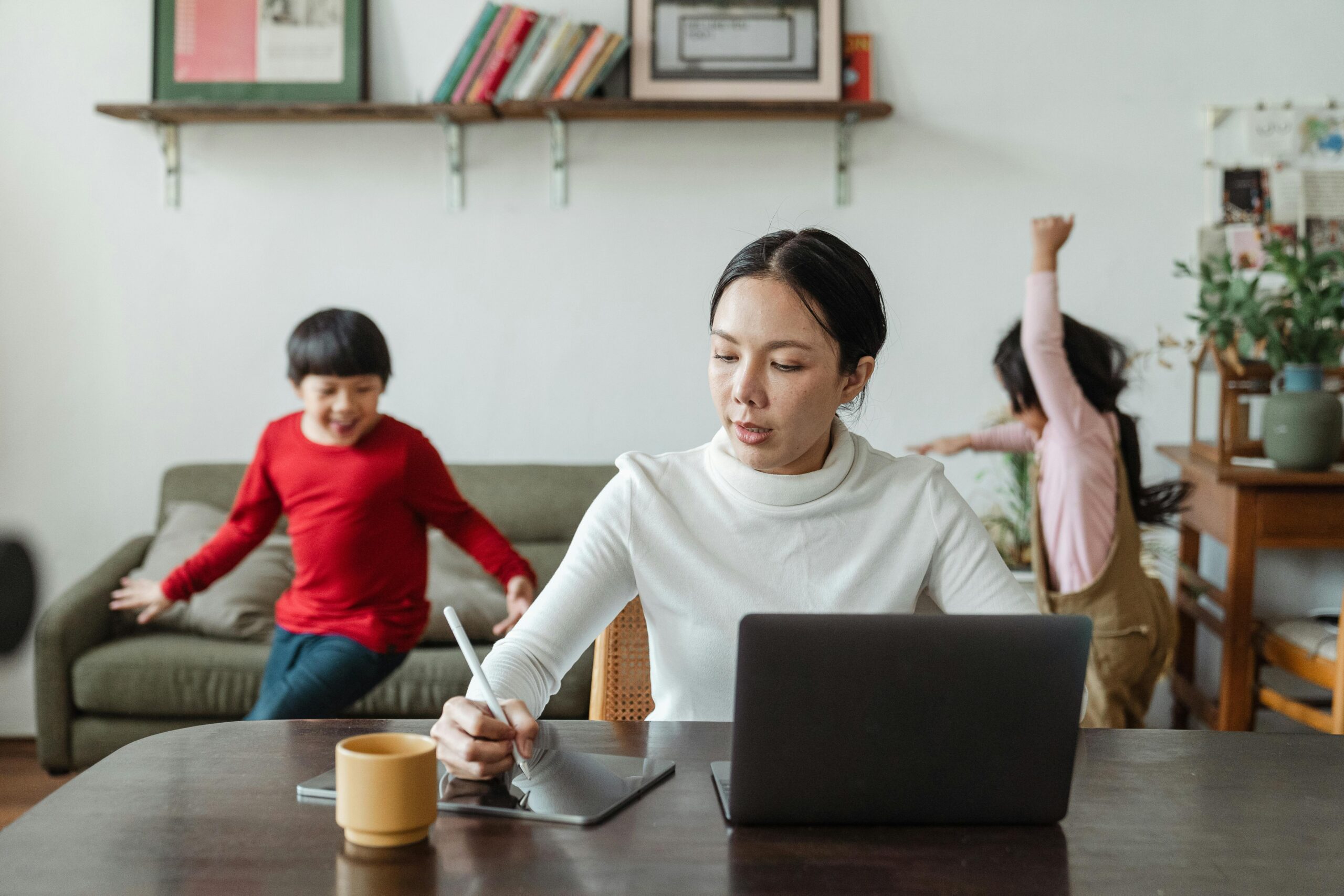 woman at table with children playing in background