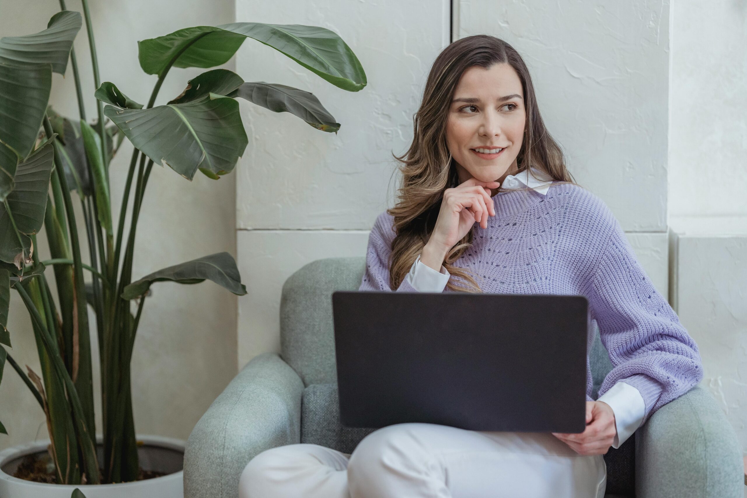 woman in purple sweater with laptop next to plant